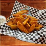 Wedge Fries - A serving basket of crispy, golden-brown wedge fries with a crunchy outside and fluffy inside, served with creamy ranch dipping sauce and a tasty snack.