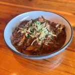 Fork and Knife Beef Stew - A bowl of Barrington's Fork and Knife Beef Stew — steak, carrots, celery, mushrooms, and fresh herbs in a thick Guinness and red wine broth over colcannon mashed potatoes.